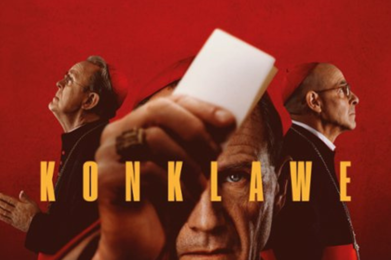 Troje mężczyzn widocznych na czerwonym tle. Aktor stojący na środku trzyma w dłoni białą kartkę w dłoni wyciągniętej przed swoją twarzą.